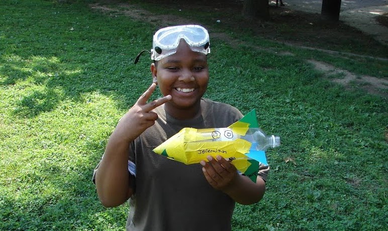 A smiling YES camper in safety goggles holding the bottle rocket he built