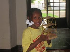 A student in a yellow YES shirt proudly holding a tower she built